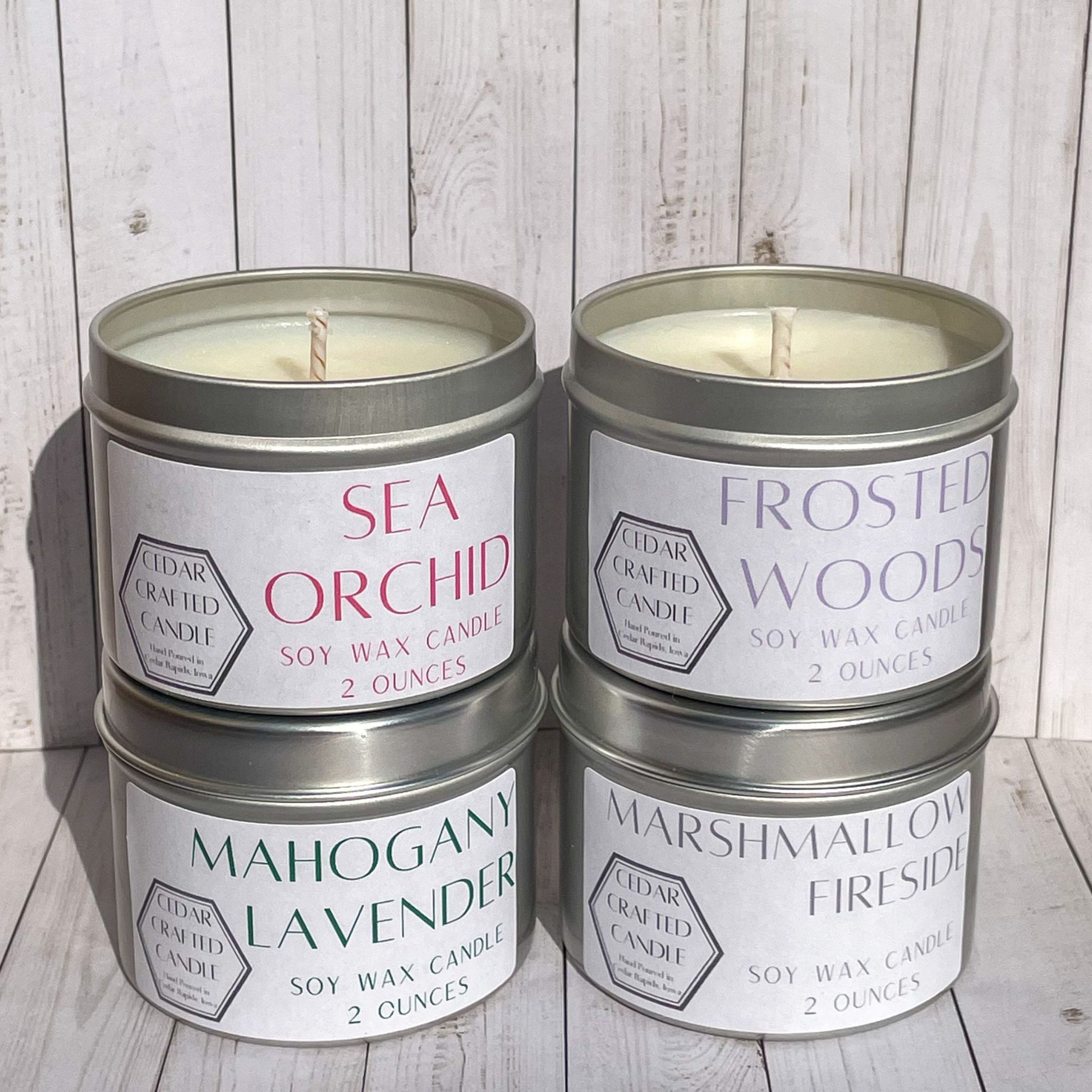 Stack of four silver candle tins with white labels.  In the scents of: Sea Orchid, Frosted Woods, Mahogany Lavender, and Marshmallow Fireside